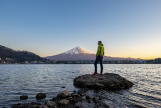 Young man standing on rocks in Lake Kawaguchi, view of Mount Fuji volcano at sunset, Yamanashi