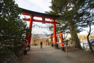 Tourist standing under red torii overlooking Mount Fuji volcano, Arakura Fuji Sengen Shrine,