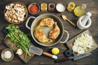 Roasted chicken legs in a pan on a wooden tabletop surrounded with mushrooms, onions, and various