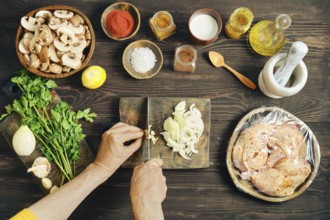 High angle view of hands chopping fresh garlic on a wooden cutting board. Chopped mushrooms,
