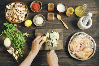 High angle view of hands slicing fresh white onion on a wooden cutting board. Chopped mushrooms,