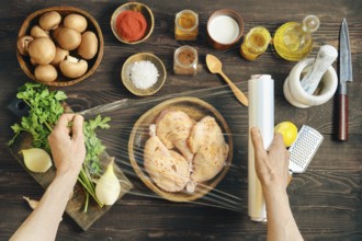 Hands wrapping marinated chicken with plastic stretch film for marinating. High angle view of