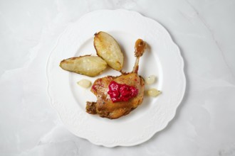 Succulent duck confit with crispy skin resting beside roasted pear caramelized in fat, garnished