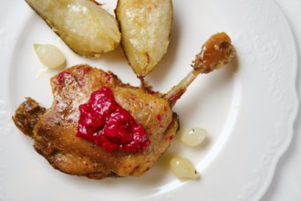Close-up view of seared duck leg on a white plate alongside roasted pears and small pearl onions. A