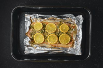 Pink salmon is placed on a baking sheet lined with foil. Lemon slices are arranged on top of the