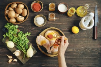 Hand sprinkle smoked paprika over raw chicken thighs making dry marinade. Other raw ingredients for