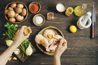 Top view of hands seasoning raw chicken thighs with curry or saffron while marinating meat on dark
