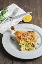 A chicken leg is placed on a gray plate. It is golden brown and garnished with green herbs. A piece