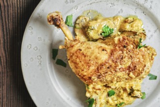 Close-up top view of roasted chicken leg on a round plate with a creamy mushroom sauce and herbs
