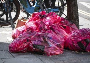 A pile of pink plastic bags with the words Trade Waste lying on the side of the road on the
