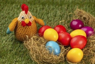 Crocheted chicken and colorful easter eggs in a nest on grass