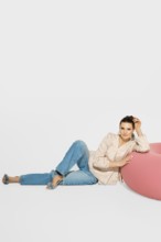 A woman is lying near a pink bean bag, leaning her torso back while resting on her left arm. She