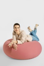 A woman lies on a pink bean bag with her legs raised and feet resting on the cushion. She wears a