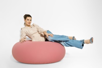 Woman is lying on a large pink lounge chair with casual clothes. The setting is a studio with
