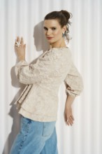 A woman leaning to the wall. She wears a light-colored outfit and shows a playful expression. The