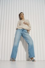 A woman stands confidently in a relaxed pose wearing wide-leg jeans and a light blouse. She is in a