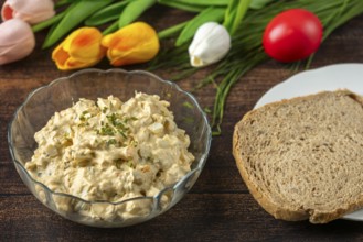 Egg salad next to a slice of bread and tulips, on rustic wooden table