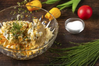 Chives fall into a bowl with ingredients for egg salad on wooden table