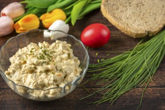 Egg salad in bowl with fresh herbs and bread, decorated with spring flowers
