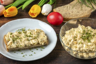Slice of bread with egg salad on plate, with fresh herbs, tulips in the background
