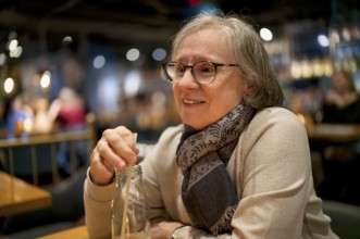 Elderly woman, portrait, glasses, gray hair, scarf, drink, straw, sitting in a bar, restaurant,