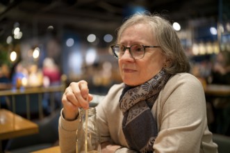 Elderly woman, portrait, glasses, gray hair, scarf, drink, straw, sitting in a bar, restaurant,