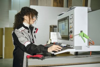 A woman is using a computer in a warehouse. She wears work gear and looks focused while interacting