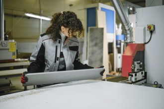 Woman working in a furniture factory inspecting a sheet of material with glued edge tape
