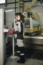 Woman stands at a control panel inside a factory, wearing protective clothing and gloves. The