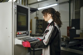 Woman launches an application for a milling machine in a furniture factory. She wears gloves and a