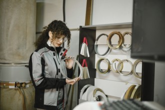 A woman stands in a workshop looking closely at a finishing edge. She is surrounded by various
