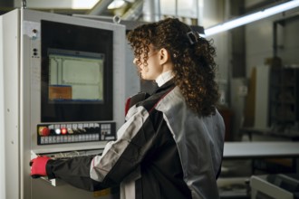 A woman is using a machine control panel in a carpentry workshop. She is focused on the screen