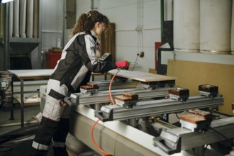 A worker blows away dust and shavings from the wooden panel using compressed air connected to a