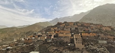 A mountainous village with many orange-colored houses in natural colors under a cloudy sky, Morocco