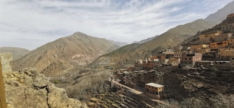 A rocky valley with a village in the mountains under cloudy sky, Atlas Mountains, Morocco