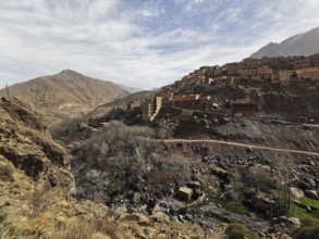 A village on a dry hill with sparse vegetation under a cloudy sky, Atlas Mountains, Morocco