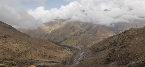 A barren mountain landscape under a cloudy sky with visible trails, Atlas Mountains, Morocco