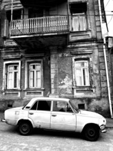 Monochrome, vintage car standing in front of a Nostaligian building with a distinctive balcony,