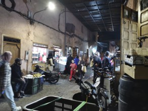 Lively, nocturnal market scene in a narrow alley of the Medina of Marrakech with people and goods,