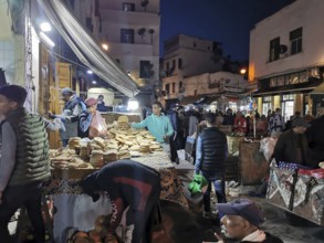 Bustling night market with bread stalls, people moving in a confined space in the Medina of