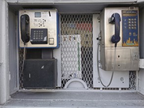 Two retro-designed telephone booths in an urban setting with metal grille and shades of gray,