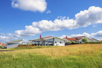 Modern residential houses with white facades and red roofs on grassy hillside under a blue sky with