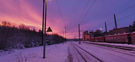 Sunrise at a snow-covered train station on Rennsteig, railroad tracks in purple sky with factory in