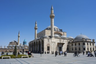 Historic mosque with several minarets under clear blue sky, people gathered in the square, Mevlânâ