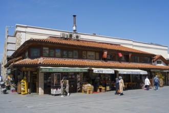Traditional market building with red tile roof surrounded by shops and people, sunny day, Konya,