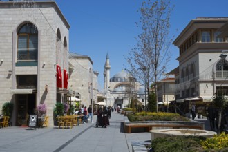 Lively shopping street with stylish buildings, mosque in the background and decorative lighting,