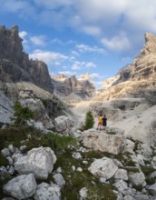 Two hikers in front of impressive mountain peaks of the Brenta Mountains, evening at Refugio