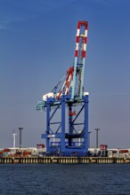 A single blue port crane, stacks of containers and a wind turbine in the background, The cranes of