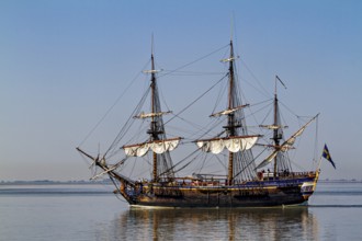 A historic sailing ship with set sails gliding calmly through the water, An old historic sailing