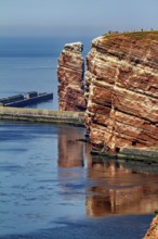 Tall red rocks rise above the sea with a protective pier, the high-seas island of Heligoland in the